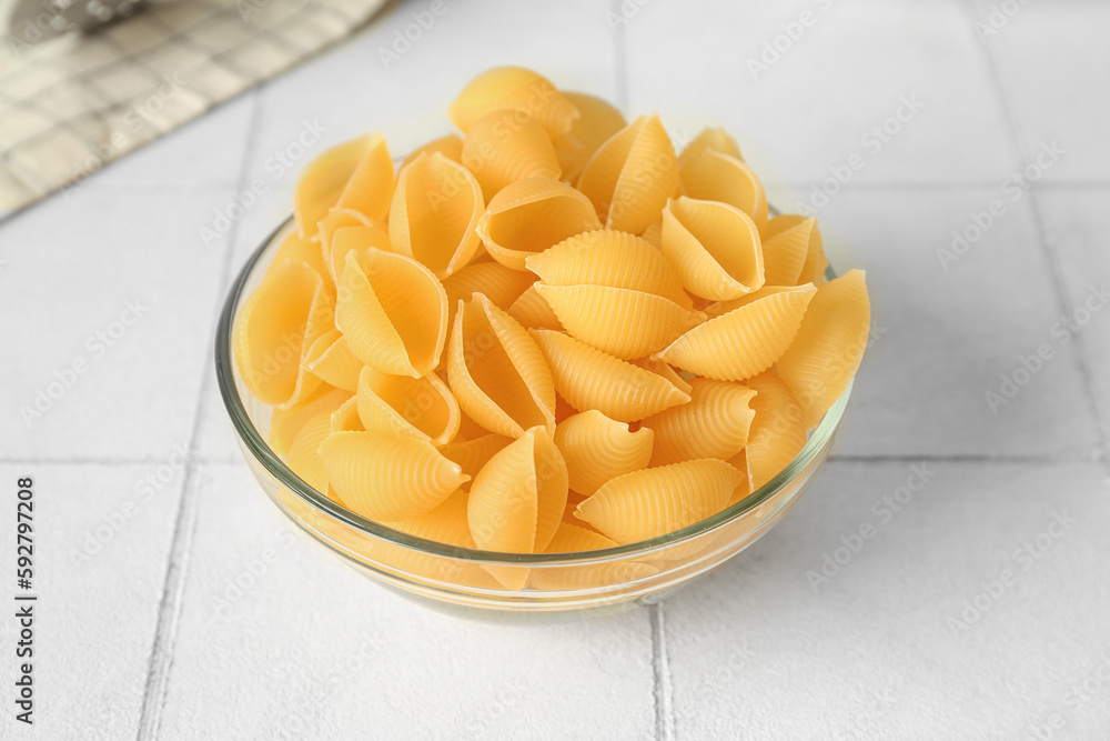 Bowl with raw conchiglie pasta on white tile background