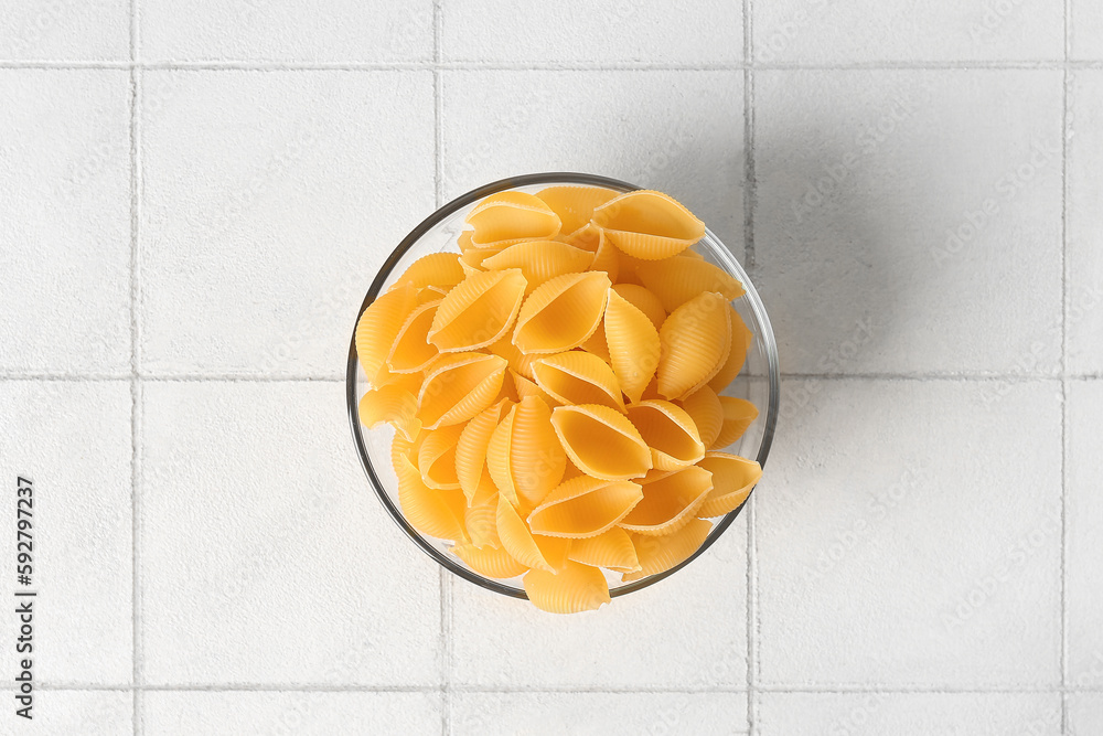 Bowl with raw conchiglie pasta on white tile background