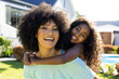 © Wavebreak Media - Portrait of smiling biracial mother carrying her happy daughter in sunny garden
