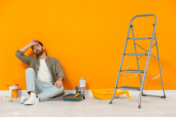 Poster - Tired designer sitting on floor near freshly painted orange wall indoors