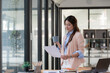 © Songsak C - Asian businesswoman reading documents while drinking coffee in an office.