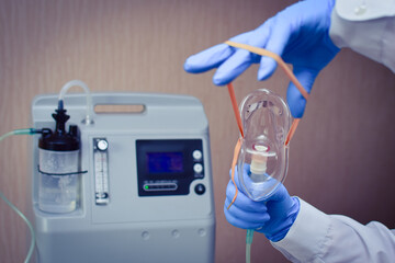 hands in medical gloves hold out an oxygen mask against the background of the oxygen generator conce