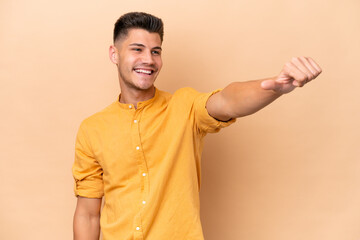 Wall Mural - Young caucasian man isolated on beige background giving a thumbs up gesture