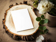 © Ann_ka - Rustic wooden slice with empty white vertical blank of paper mockup and floral greenery. Country wood ring with flat card for wedding invitation or greeting on the table. Generative AI