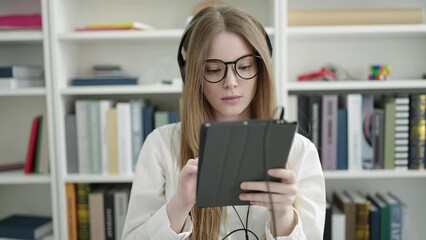 Wall Mural - Young blonde woman student using touchpad and headphones studying at university classroom