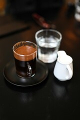 Poster - Black table with a cup of coffee, a portion of milk and a cup of water