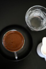 Wall Mural - Black table with a cup of coffee, a portion of milk and a cup of water