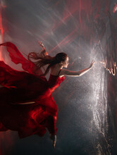 Fantasy Mystery Woman Swims Underwater Touches Magic Light Mirror, Looks Into Reflection. Fairy Tale Beauty Girl Princess Sleeping Soars Floating In Dream Dark Water. Art Ballerina Dancing Red Dress