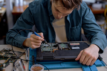 Wall Mural - caucasian professional IT specialist replacing details in computer repair workshop, hardware upgrading. A real case of service assistance. Concentrated male sit at work place repairing old laptop