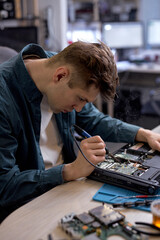 Wall Mural - Young caucasian man disassembles broken laptop. Computer service and repair concept. Laptop disassembling in repair shop, workshop. Electronic development by professional technician