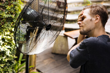 Fototapete - Heat wave during a summer, a man finds respite at his home balcony with the help of an electric fan. A man beats the summer heat wave by finding relief with an fan. The effect of global warming