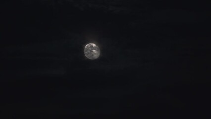 Wall Mural - Time lapse video of a bright moon in the sky at night covered by clouds