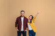 © Moon Safari - Cheerful young girlfriend with hand raised screaming and leaning on handsome boyfriend. Portrait of attractive couple dressed in shirts posing happily over beige background