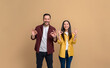 Young woman and man dressed in shirts laughing and showing OK signs while posing against beige background. Portrait of couple looking at camera and gesturing cheerfully