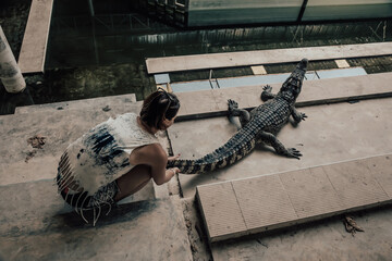 A girl sits next to a crocodile in an abandoned building. Abandoned crocodile farm. Scary crocodile. Young beautiful girl.