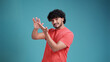 © Виталий Лысак - Young handsome Indian man with beard in coral t-shirt on blue studio background doing money gesture with hands, asking for salary payment