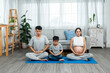 © Ekkasit A Siam - Asian parent and son sitting in yoga meditation pose in living room. son follows father in yoga poses. Pregnant mother wearing a tank top reveals stomach, woman relaxing while pregnant