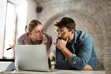 Young businessman talking to his female colleague while working on laptop in the office