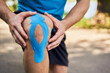 © baranq - Close-up of male runner holding injured knee with kinesiology tape. Kinesiotaping concept