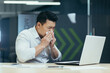 © Liubomir - A young sick Asian man is sitting at work in the office. He wipes his nose from a runny nose with a napkin, coughs, feels bad.