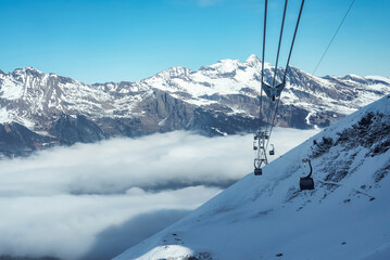 Wall Mural - Gondola lifts moving on cables over snow covered hill with beautiful snowcapped Bernese mountains under sky at ski resort in Jungfrau, Switzerland, winter holiday and nature concept