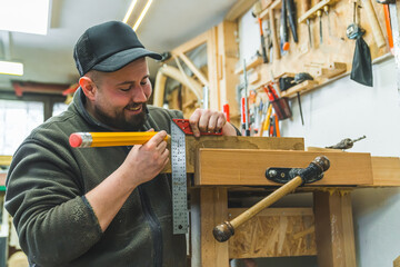 Happy male carpenter marking on wood with big pencil. Variety of tools used in carpentry - bracket and vise. High quality photo