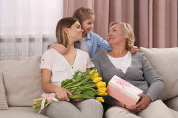 Wall Mural - Little girl congratulating her mom and granny with flowers and gift at home. Happy Mother's Day