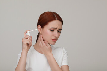 Canvas Print - Unhappy woman using ear spray on light grey background. Space for text