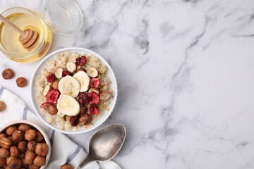 Delicious oatmeal with freeze dried berries, banana and hazelnuts served on white marble table, flat lay. Space for text