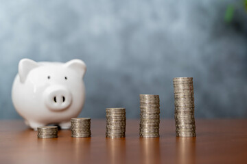 Piggy bank with coins on old wooden table. stack of coins and white smiling piggy bank for growth and saving with money box Saving money for future plans