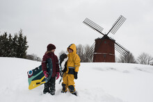 Kids Sledging In The Snow Next To A Windmill