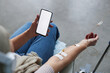 © Seventyfour - Close up of woman holding smartphone with white screen mockup during IV drip treatment, copy space