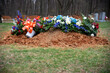 Newly buried grave with dirt and flowers in grassy cemetery