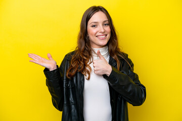 Wall Mural - Young caucasian woman isolated on yellow background holding copyspace imaginary on the palm to insert an ad and with thumbs up