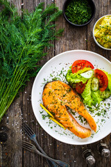 Fried salmon steak and fresh vegetable salad served on wooden table
