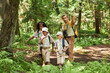© Seventyfour - Group of scouts hiking in forest with adult leader pointing away, copy space