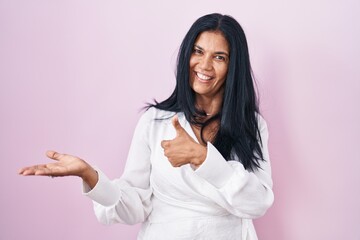 Sticker - Mature hispanic woman standing over pink background showing palm hand and doing ok gesture with thumbs up, smiling happy and cheerful