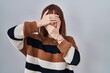 © Krakenimages.com - Young beautiful woman wearing striped sweater over isolated background covering eyes and mouth with hands, surprised and shocked. hiding emotion