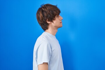 Poster - Hispanic young man standing over blue background looking to side, relax profile pose with natural face and confident smile.