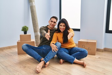 Canvas Print - Young couple sitting on the floor at new home smiling friendly offering handshake as greeting and welcoming. successful business.