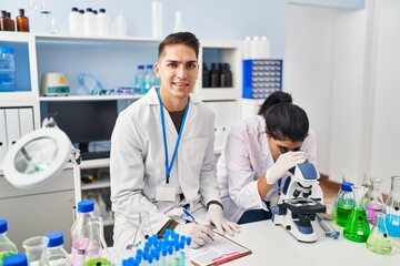 Wall Mural - Man and woman scientists partners using microscope working at laboratory