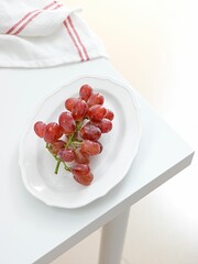 Canvas Print - Vertical shot of red grape in a white plate with a kitchen towel on a table