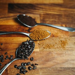 Poster - Closeup shot of coffee beans and ground coffee on spoons on a wooden surface