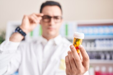 Sticker - Young hispanic man pharmacist looking pills bottle at pharmacy