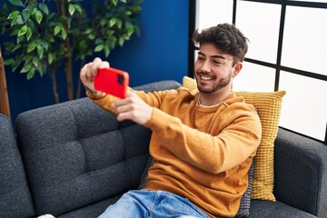 Canvas Print - Young hispanic man make selfie by smartphone sitting on sofa at home