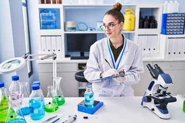 Poster - Young woman scientist measuring liquid writing on document at laboratory