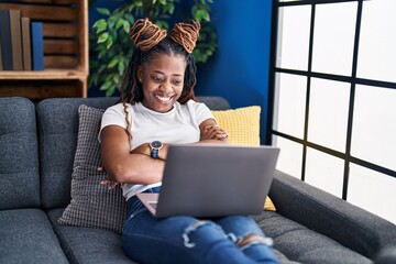 Sticker - African woman with braided hair using laptop at home happy face smiling with crossed arms looking at the camera. positive person.