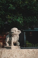 Sticker - Vertical shot of a Chinese lion sculpture in the park with trees in the background