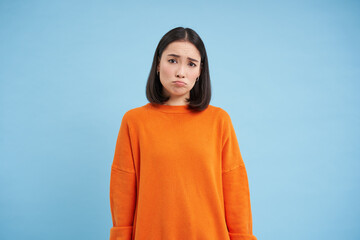 Wall Mural - Miserable asian girl, sulks and looks sad, frowns and pouts disappointed, feels like loser, stands over blue background
