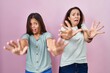 © Krakenimages.com - Young mother and daughter standing over pink background afraid and terrified with fear expression stop gesture with hands, shouting in shock. panic concept.